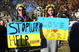 protesters holding signs that say, "Stop War, Help Ukraine" and "Love not War"