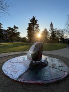 Image of the Albion College rock with the sun setting over it. One side of the rock is white and the other black with the words “Women Life Freedom.”